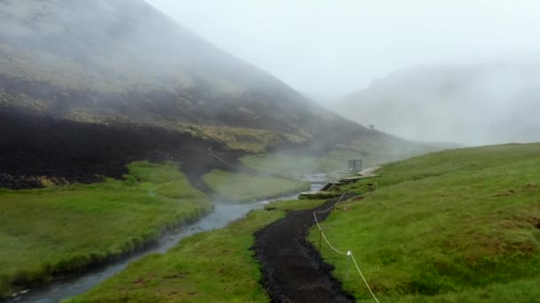 Vista aérea do vale de Reykjadalur com rio de fontes termais e piscina com prado de grama verde exuberante e colinas com vapor geotérmico. Vista drone de banho em fontes termais na Islândia — Vídeo de Stock