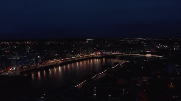 Vista panorámica aérea del puente iluminado y el paseo marítimo en la ciudad. Luces reflectantes superficiales. El río Shannon fluye tranquilamente en la ciudad nocturna. Limerick, Irlanda — Vídeo de stock