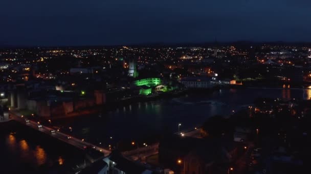 Volar por encima de la ciudad de la noche, verde iluminado gran edificio en Shannon ribera del río. Limerick, Irlanda — Vídeo de stock