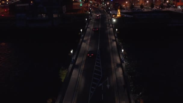 Seguimiento hacia adelante de los coches que conducen en el puente de carretera a través del río Shannon. Vista aérea de las calles de la ciudad nocturna. Limerick, Irlanda — Vídeo de stock