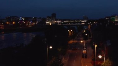 Nehir kenarındaki Shannon caddesinin üzerinde uçuyorlar. Köprü ve diğer kıyıda aydınlatılmış rıhtım. Limerick, İrlanda