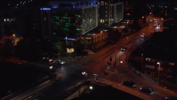 Erhöhte Aufnahme von Autos, die durch eine Kreuzung in der nächtlichen Stadt fahren. Farbig beleuchtetes Gebäude an Ecke. Limerick, Irland — Stockvideo