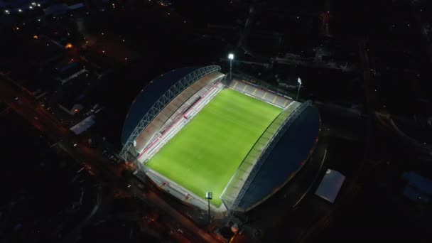 Vuela alrededor del estadio de fútbol por la noche. Vista de ángulo alto del campo de juego verde vacío brillantemente iluminado, lugar de deportes en la ciudad. Limerick, Irlanda — Vídeo de stock