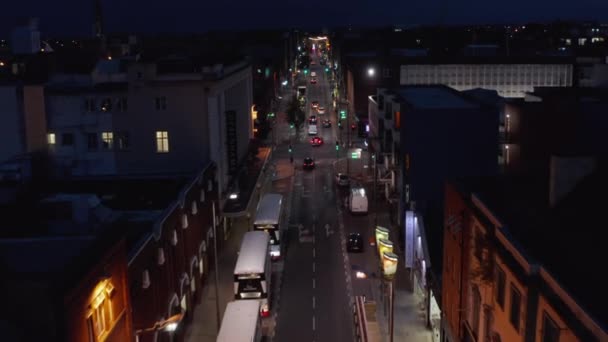 Seguimiento hacia adelante del grupo de coches que conducen en una calle de sentido único en la ciudad nocturna. Carretera bordeada por vehículos aparcados y casas adosadas. Limerick, Irlanda — Vídeo de stock