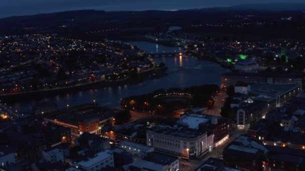 Vuela por encima de la ciudad por la noche. Vista aérea del río que fluye a través de la ciudad nocturna con luces de calle. Limerick, Irlanda — Vídeo de stock