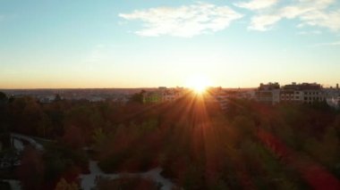 Kamu parkındaki apartmanların arkasına saklanan parlak batan güneşe karşı uçmak. Akşam romantik manzarası.