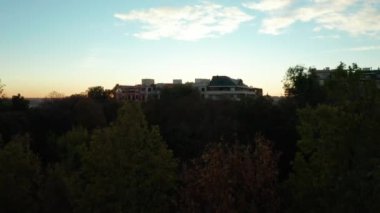 Parktaki ağaçların üzerinden uçar, apartman dairelerini gözler önüne serer ve şehrin üzerine güneş doğar..