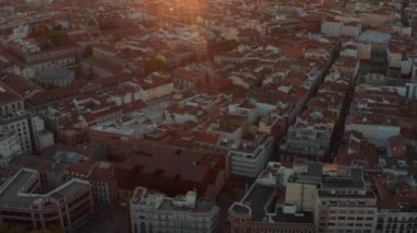 Büyük şehrin merkezine doğru uç. Kırmızı çatıları olan çeşitli binaların havadan panoramik görüntüsü. Yukari egilmek sehri ortaya çikarir ve günes ufukta batar.