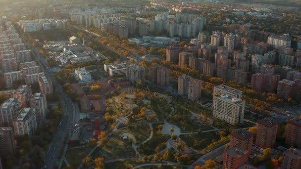 Tiro aéreo de parque cercado por casas de apartamento de vários andares na propriedade de alojamento. Árvores coloridas iluminadas pelo pôr do sol. — Vídeo de Stock