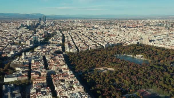 Zdjęcia lotnicze z dużej metropolii. Bloki budynków oddzielone ulicami. Duży zielony park El Retiro z widokami i powierzchnią wody. — Wideo stockowe