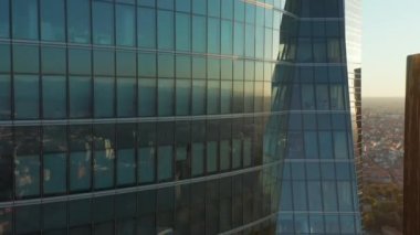 Pencereler boyunca yükselen görüntüler ve ofis gökdeleninin cam duvarı kasabadaki binaları ve güneşi yansıtıyor. Damdaki İspanyol bayrağı gözler önüne seriliyor.