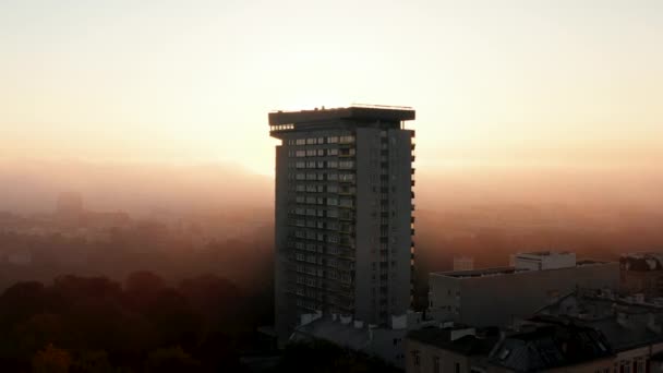 Летать над автономным высоким жилым домом в городе. Раскрытие восходящего солнца в тумане. Утренний выстрел сквозь туман или низкие облака. Уорсоу, Польша — стоковое видео