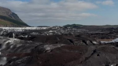 Breidamerkurjokull buzulunun dili ve etrafındaki volkanik dağların muhteşem drone görüntüsü. Vatnajokull Ulusal Parkı 'nda volkanik kaya oluşumlarının kuş gözü ve donmuş buzullar.