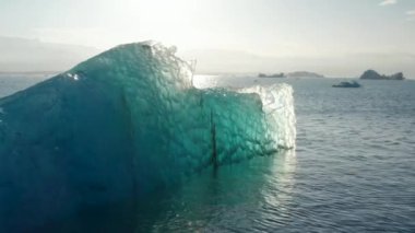 İzlanda 'daki Breidamerkurjokull buzulunun güneşli bir gününde parlayan buzdağının insansız hava aracı görüntüsü. Gökyüzü manzarası, mavi renkler, ilginç şekiller ve desenlerle aydınlatılmış buzdağı.