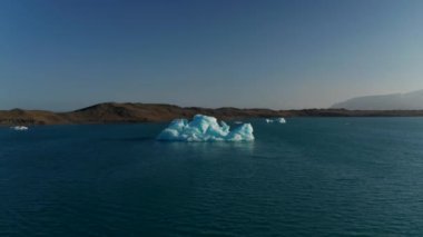 İzlanda 'daki Vatnajokull Ulusal Parkı' ndaki Jokulsarlon Gölü 'nde yüzen buzdağının etrafında dönen kuş gözü dronu. Küresel ısınma İklim değişikliği. İnsansız hava aracı görüntüsü buz bloğu İzlanda gölünde eriyor