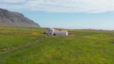 Panoramik drone manzaralı güzel manzaralı İzlanda 'da eski bir ev. İzlanda 'nın otlak arazilerindeki çiftlik evinin havadan görünüşü. İzlanda 'nın kırsal kesimindeki ıssız kırmızı çatı evi.