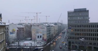 Şehir merkezindeki cadde kavşağı çevresindeki binaların yüksek görüntüsü. Arka planda inşaat alanında bir grup vinç var. Kar yağışlı kış havası. Berlin, Almanya
