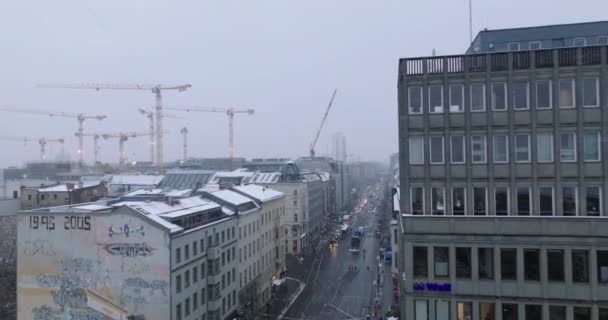 Fliegen Sie im Winter über Straßen in Stadtvierteln. Gruppe von Turmdrehkranen auf der Baustelle. Fallender Schnee bedeckt mehrstöckige Hausdächer. Berlin, Deutschland — Stockvideo