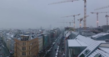 Şehirdeki yeni çok katlı binanın şantiyesinde çalışan yüksek kuleli vinçler. Kış şehrinde sokağın üzerinden uç. Berlin, Almanya