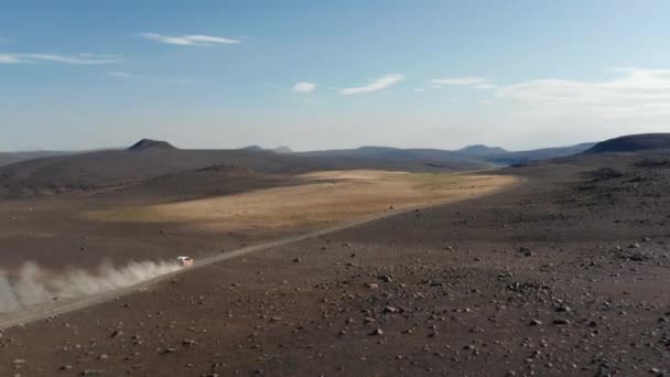 Disparo aéreo después de un coche que agita una gran nube de polvo a medida que avanza a lo largo de una carretera desértica polvorienta. Drone vista vehículo exceso de velocidad en camino de polvo en Islandia explorar paisaje increíble — Vídeo de stock