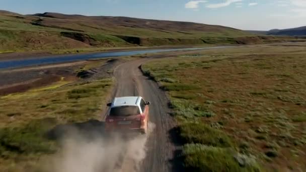 Drone view car driving riverside in Iceland mossy and muddy countryside. Aerial view 4x4 vehicle exploring icelandic highlands driving near river stirring up dust cloud. Freedom and wanderlust — Stockvideo