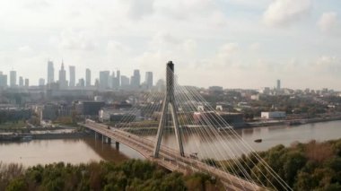 Nehir boyunca uzanan güzel modern tasarım köprüsünün kayan ve pan görüntüsü. Arka planda yüksek katlı ofis binaları olan bir siluet. Varşova, Polonya
