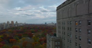 İleri doğru yüksek binalar boyunca uçar. Kasaba binalarıyla çevrili büyük parkın görüntüsü. Sonbahar rengarenk Central Park. Manhattan, New York City, ABD