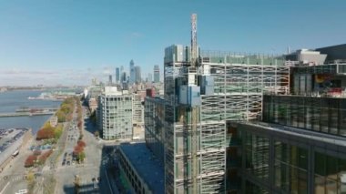 Rıhtımdaki yeni binadaki inşaat alanının etrafında uçun. İnşaat asansörü kalkıyor. Modern gökdelenlerle gökyüzü aydınlanıyor. Manhattan, New York City, ABD