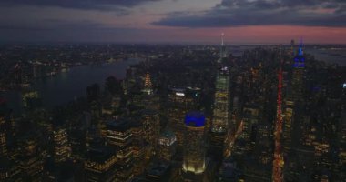 Gün batımında şehir merkezinin hava panoramik görüntüleri. Yüksek binaların ışıklı pencereleri ve renkli alacakaranlık gökyüzü. Manhattan, New York City, ABD