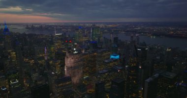 Alacakaranlıktaki büyük şehirdeki gökdelenlerin hava panoramik görüntüleri. Işıklı pencereler ve gökdelenlerin renkli çatıları. Manhattan, New York City, ABD