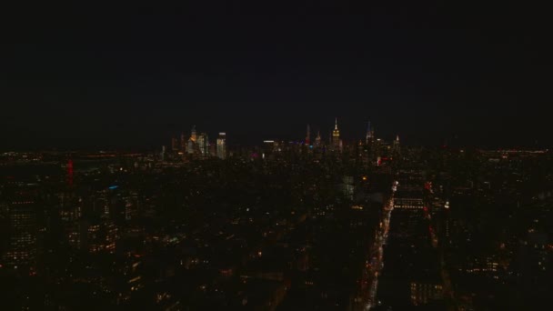 Forwards fly above urban neighbourhood at night. Cityscape with illuminated downtown skyscrapers in distance. Manhattan, New York City, USA — Stock Video