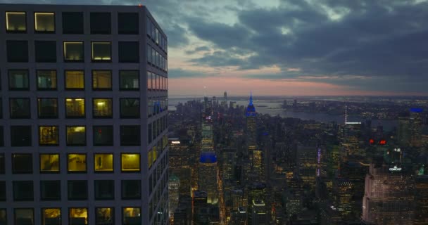 Strak vliegen boven de bovenste verdiepingen van de moderne wolkenkrabber torent boven de stad. Onthul panoramische opname van het centrum in de schemering. Manhattan, New York City, Verenigde Staten — Stockvideo