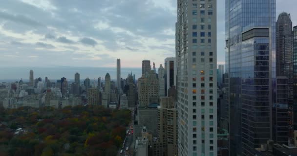 Slide e pan tiro de arranha-céus edifícios do centro da cidade e rua longa movimentada levando sobre Central park. Arranha-céus modernos refletindo o céu crepúsculo. Manhattan, Nova Iorque, EUA — Vídeo de Stock