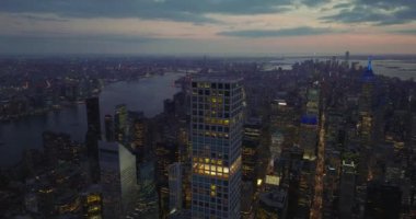 Şehir merkezinde, su yüzeyiyle çevrili yüksek gökdelenlerin akşam panoramik görüntüleri. Renkli alacakaranlık gökyüzü. Manhattan, New York City, ABD