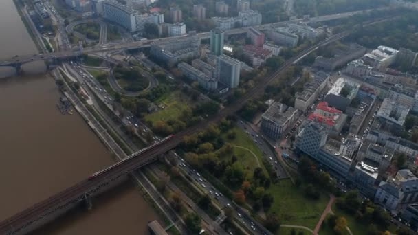 Şehirdeki trafiğin yüksek açılı görüntüsü. Yoğun rıhtım yolu ve Vistula nehri boyunca giden yolcu treninin izini sürüyorum. Varşova, Polonya — Stok video