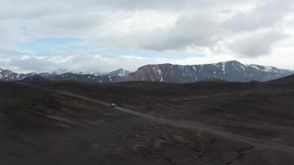 Top vista carro condução deserto terreno vulcânico preto acelerando em terras altas Islândia. Vista aérea do drone do campo icelandic surpreendente com pico nevado das montanhas e panorama preto vulcânico da areia — Vídeo de Stock