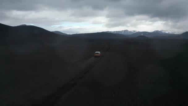 Légi felvétel drón követő autó gyorsan halad a fekete láva terep útvonalon Izlandon. Lenyűgöző panoráma a jéggel fekete vulkanikus táj. Biztonsági és biztosítási koncepció — Stock videók