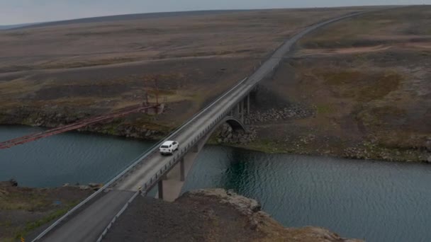 Vista aérea de un puente que cruza un río que fluye a través de las tierras altas de hielo. Drone vista coche conduciendo por el puente con agua dulce corriendo debajo. Islandia paisaje — Vídeos de Stock