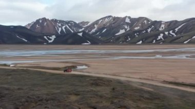İnsansız hava aracı yüksek kar zirvesi olan İzlanda kırsalının muhteşem manzarası. 4x4 off-road aracının kuşbakışı görüntüsü İzlanda dağlık arazilerindeki toprak yolda hız yapıyor.