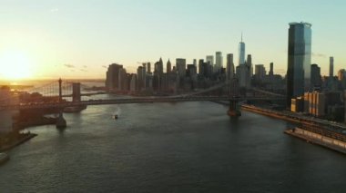 İleri, nehrin üzerinden uçar. Gün batımında asma köprüler. Modern yüksek gökdelenleri olan bir gökyüzü. Yollarda yoğun trafik var. Manhattan, New York City, ABD