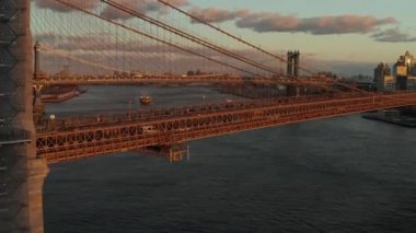 Brooklyn Köprüsü 'nün destek kablolarının üzerinden uç. Manhattan Köprüsü 'nün altından geçen kargo teknesinin hava görüntüsü. Şehirde günbatımı. Brooklyn, New York City, ABD