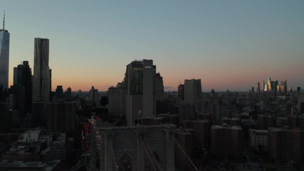 Vola intorno alla bandiera americana issata sulla torre del ponte. Strada multilane occupato in città a polvere e grattacieli del centro che riflettono il sole tramontante in lontananza. Manhattan, New York, USA — Video Stock