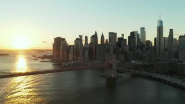 İleri, nehrin üzerinden uçar. Parlak günbatımı gökyüzüne karşı Brooklyn Köprüsü 'nün havadan görüntüsü. Finans Bölgesi 'ndeki gökdelenler. Manhattan, New York City, ABD