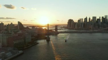 Güneş batarken Manhattan Köprüsü 'nün altından geçen yolcu gemisinin hava görüntüsünü alıyorum. Arka planda rıhtımdaki gökdelenler. Manhattan, New York City, ABD