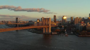 Büyük asılmış köprü batan güneş tarafından aydınlatılır. Yolcu gemisi Brooklyn Köprüsü 'ne gidiyor. Rıhtımdaki binalar. Brooklyn, New York City, ABD