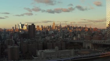 Nehir kenarındaki köprülerin ve rıhtımların ortaya çıkışı. Akşam güneşiyle aydınlatılmış yüksek gökdelenleri olan şehir manzarası. Manhattan, New York City, ABD