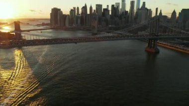 Gün batımında nehrin üzerindeki büyük asma köprülerin inanılmaz görüntüleri. Modern gökdelenlerle gökdelenlerin yükselişini göster. Manhattan, New York City, ABD