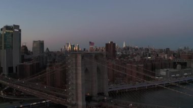 Brooklyn Köprüsü 'nün etrafında Amerikan bayrağıyla dalgalanan forvetler. Alacakaranlıkta apartmanı olan bir yerleşim yeri. Uzaktan aydınlatılmış gökdelenler. Manhattan, New York City, ABD