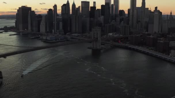 Aerial view of Brooklyn Bridge spanning East river at dusk. Tilt up reveal of skyline with modern business skyscrapers against colourful sunset sky. Manhattan, New York City, USA — Vídeo de Stock