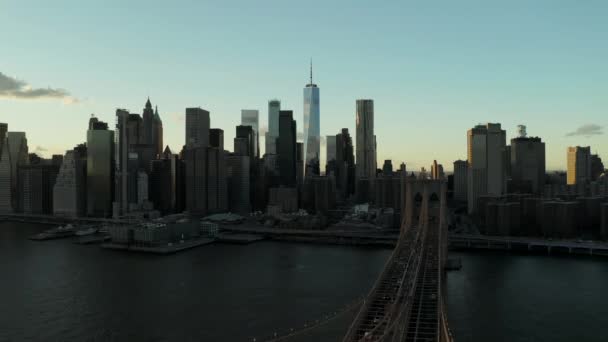 Aerial view of historic bridge spanning river and cityscape with modern skyscrapers. Backwards reveal of stone suspension tower with American flag on top. Manhattan, New York City, USA — Stockvideo